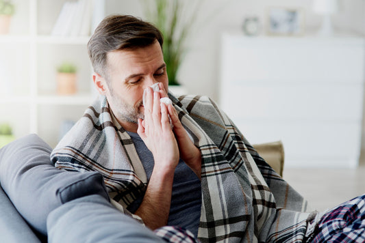 A man with flu symptoms sitting on a sofa and sneezing.