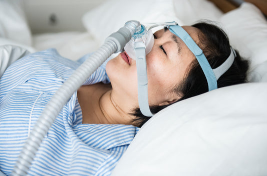 Kuvassa henkilö makaa sängyllä CPAP-maski kasvoillaan.